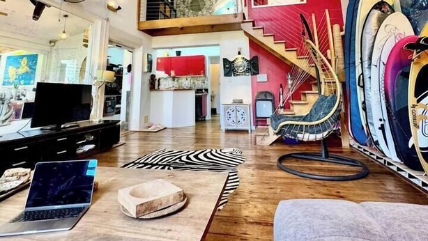 A spacious living area with a high ceiling, a staircase, a TV, and a laptop on a table.