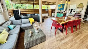 A spacious living area with a sofa, a dining table with red chairs, and a kitchen area with a counter and various items.
