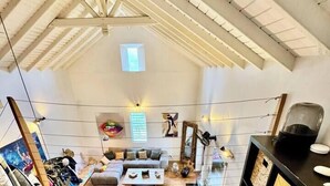 A spacious loft with a high ceiling, a glass coffee table, a zebra-patterned rug, and a modern living area with a sofa and a TV.
