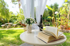 Un jardin, avec une table, un livre, une bouteille de vin et un vase de fleurs.