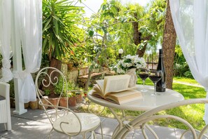 An outdoor patio with a table, chairs, an open book, a bottle, and a vase of flowers.