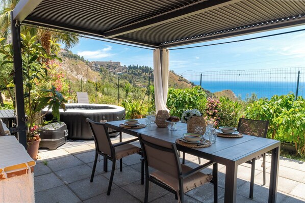An outdoor patio with a table set for dining, surrounded by greenery and overlooking a scenic view.