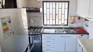 A compact kitchen with white cabinets, a gas stove, a sink, and a window with bars.