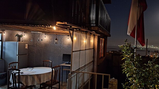 An outdoor dining area with a table and chairs, a small computer on a table, and string lights.