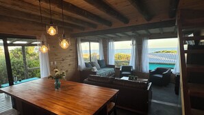 Interior em madeira com uma mesa de jantar, cadeiras, um sofá e vista para o mar.
