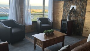 Uma sala de estar acolhedora, com teto de madeira, lareira, televisão e vista para a praia e montanhas.