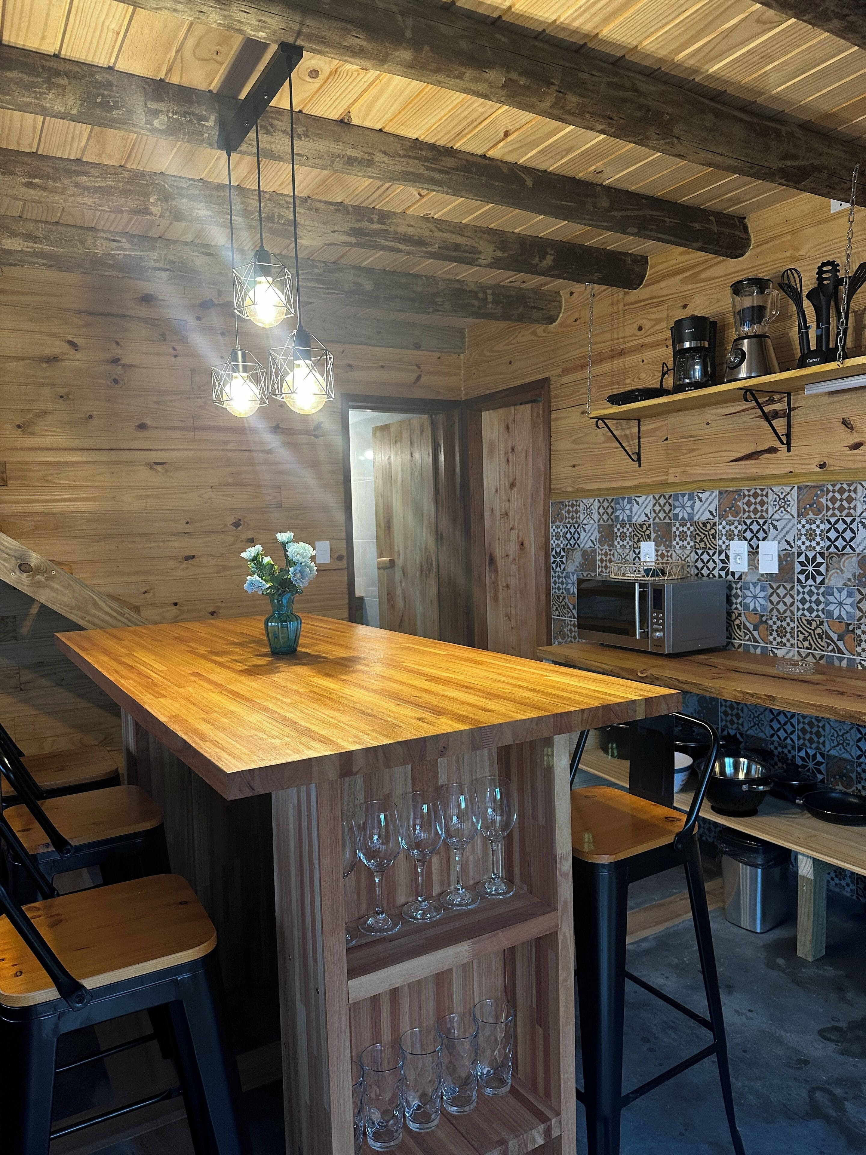 A wooden kitchen with a wooden island, hanging light fixtures, and a tiled backsplash.