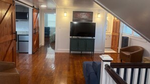 Amplia sala de estar con piso de madera, televisor sobre un mueble y una escalera que conduce a otra habitación.