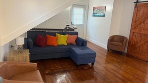 Una sala de estar con un sofá seccional azul, una mesa de centro de madera, un sillón de cuero marrón y piso de madera.