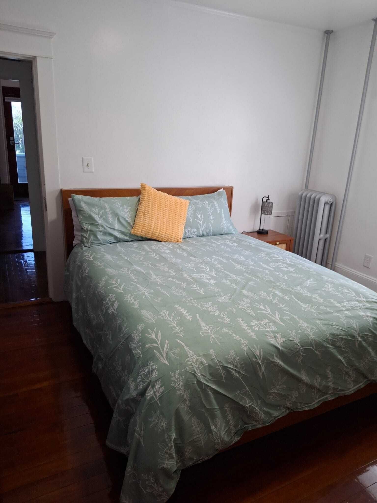 Un dormitorio con cama, mesita de noche, lámpara y radiador.