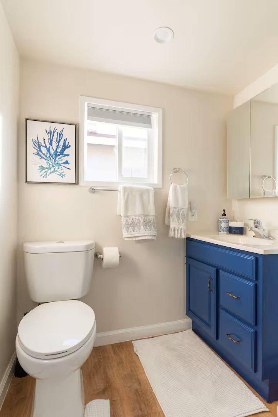 A bathroom with a toilet, a sink, a window, and a blue cabinet.