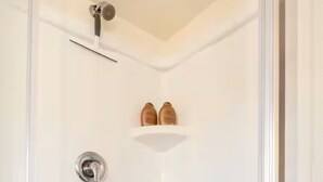Une cabine de douche fermée par des parois en verre, dotée d’un pommeau de douche à main, d’un porte-savon et de deux bouteilles de shampoing posées sur une étagère.