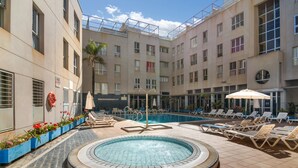 A pool area with lounge chairs, a hot tub, and a building with multiple floors and windows.