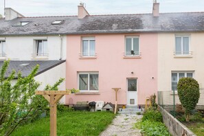 A two-story residential building with a pink and white facade, a small front garden, and a wooden pergola.