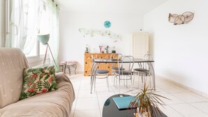 A living room with a sofa, a coffee table, a dining table with chairs, a wooden cabinet, and a wall clock.