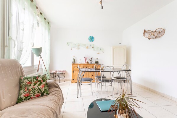 A living room with a sofa, a coffee table, a dining table with chairs, a wooden cabinet, and a wall clock.