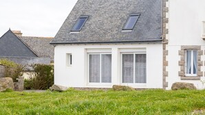 Une maison avec un toit en pente, deux fenêtres avec volets et une façade blanche.
