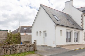 A white building with a sloped roof, a stone wall, and a paved driveway.