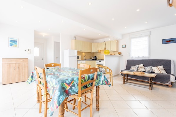 A modern kitchen with wooden cabinets, a dining table with chairs, and a sofa in a bright living area.