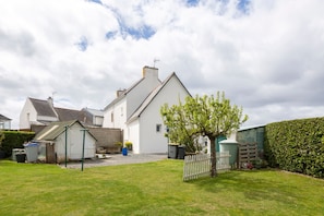 A residential property with a white house, a fenced yard, and a hedge.