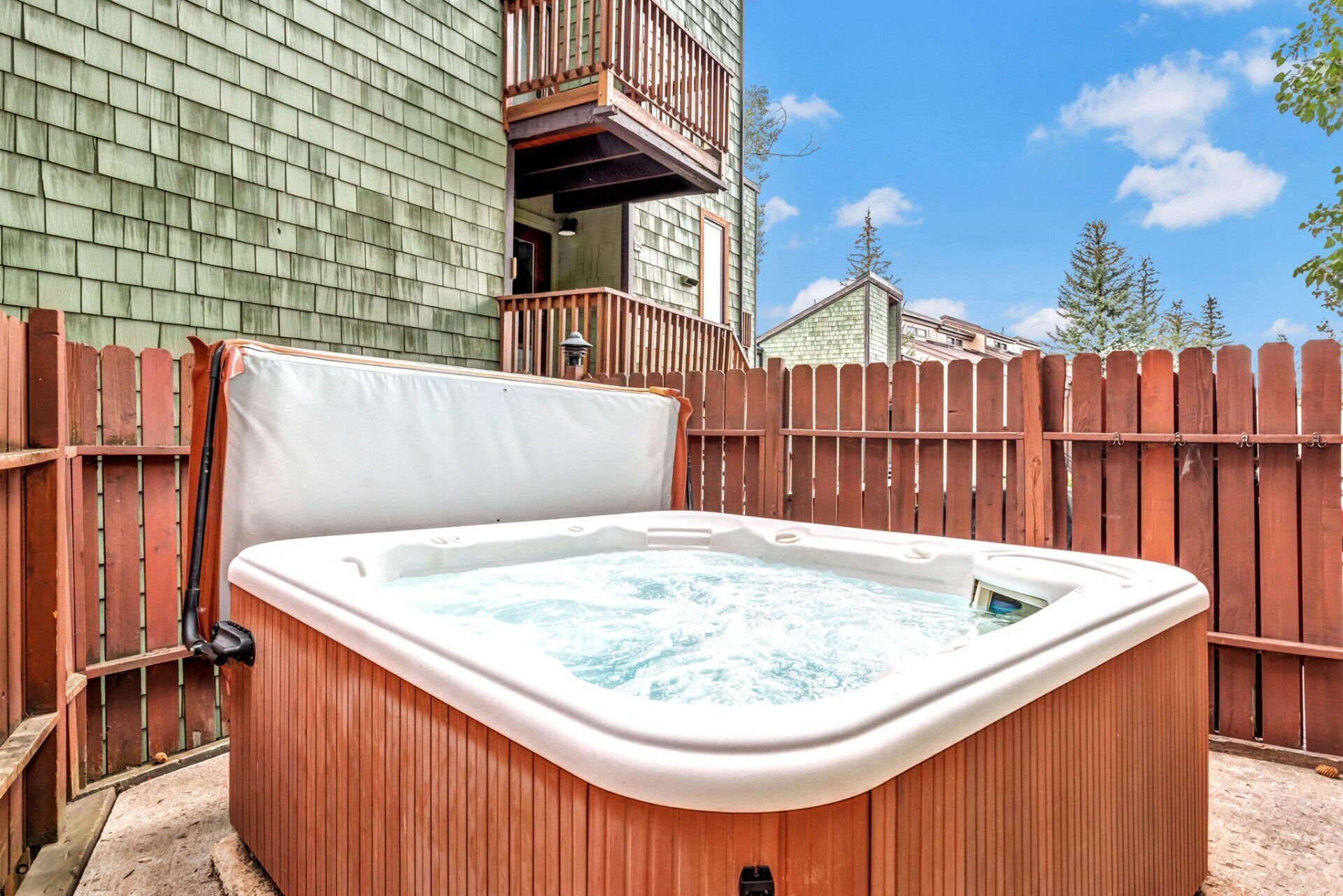 A hot tub in a backyard with a wooden fence and a building in the background.