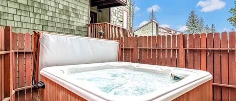 A hot tub in a backyard with a wooden fence and a building in the background.