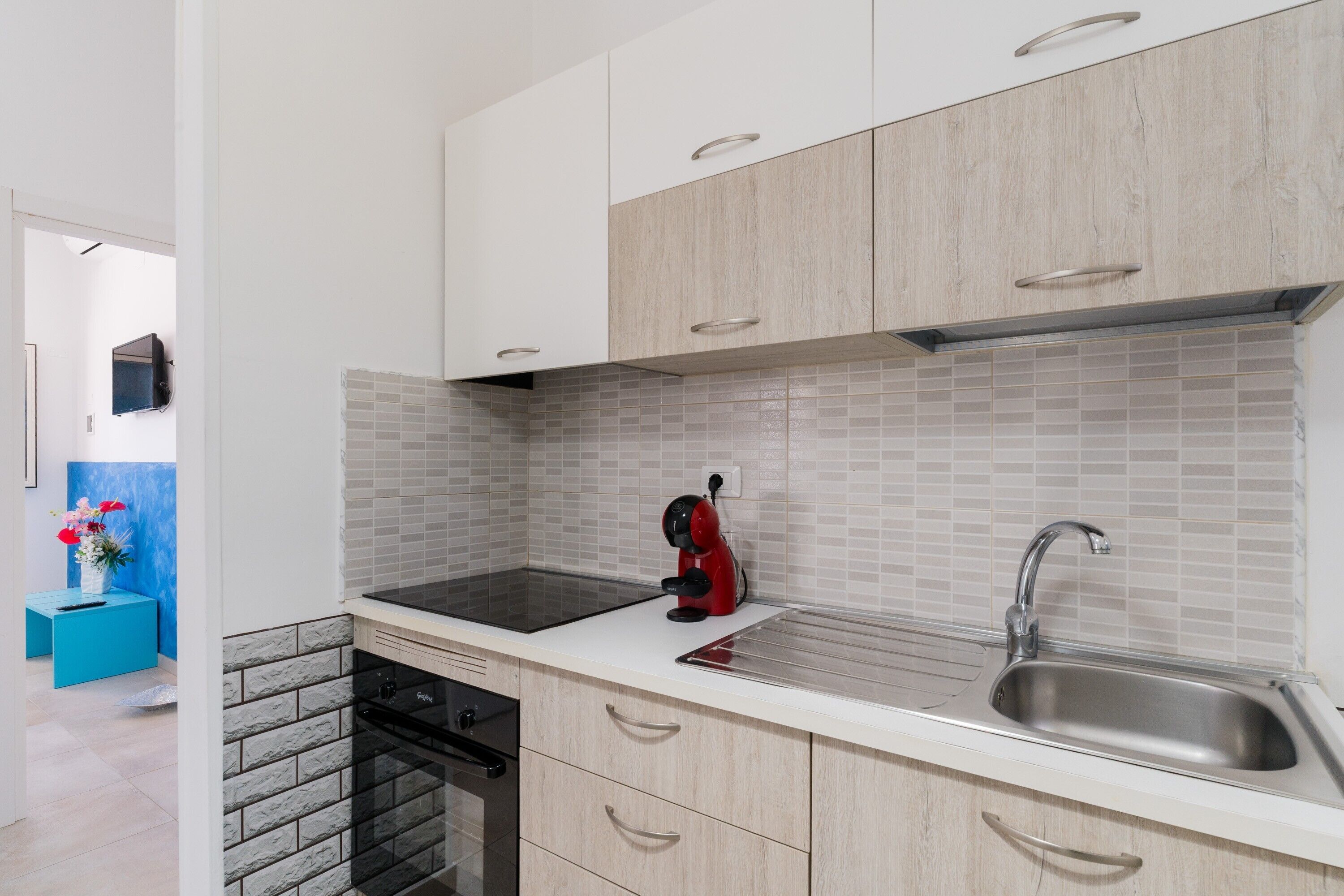 Une cuisine moderne avec un fourneau noir, un évier et une bouilloire rouge.