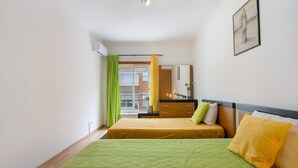 Ein Hotelzimmer mit zwei Betten, einer grünen Tagesdecke, einem gelben Kopfkissen und Blick ins Freie.