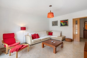 Un salon avec un canapé, un fauteuil rouge, une table basse et un luminaire suspendu.
