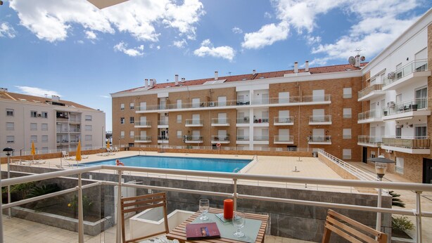 Ein Balkon mit Pool, Tisch und Stühlen sowie Blick auf ein mehrgeschossiges Gebäude mit Balkonen.