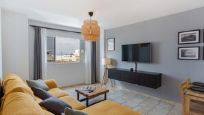 A modern living room with a sofa, a coffee table, a TV mounted on the wall, and a window with curtains. - Vacation 'El Pico' with Wi-Fi (La Santa)