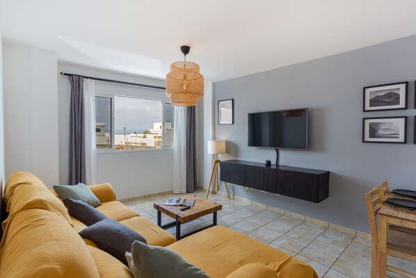 Ein modernes Wohnzimmer mit einer Couch, einem Couchtisch, einem an der Wand montierten Fernseher und einem Fenster mit Vorh ängen.