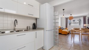 A modern kitchen with white cabinets, a stainless steel sink, and a refrigerator. There is a dining area with a wooden table and chairs. - Vacation 'El Pico' with Wi-Fi (La Santa)