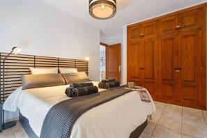 Ein Schlafzimmer mit Bett, Nachttischlampen, einem Holzschrank und Blick auf einen Flur.