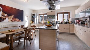 A modern kitchen with a central island, wooden dining table, and chairs. - Room 'Ortlersuite Zi 4' with Mountain View, Shared Garden and Balcony (Schluderns)