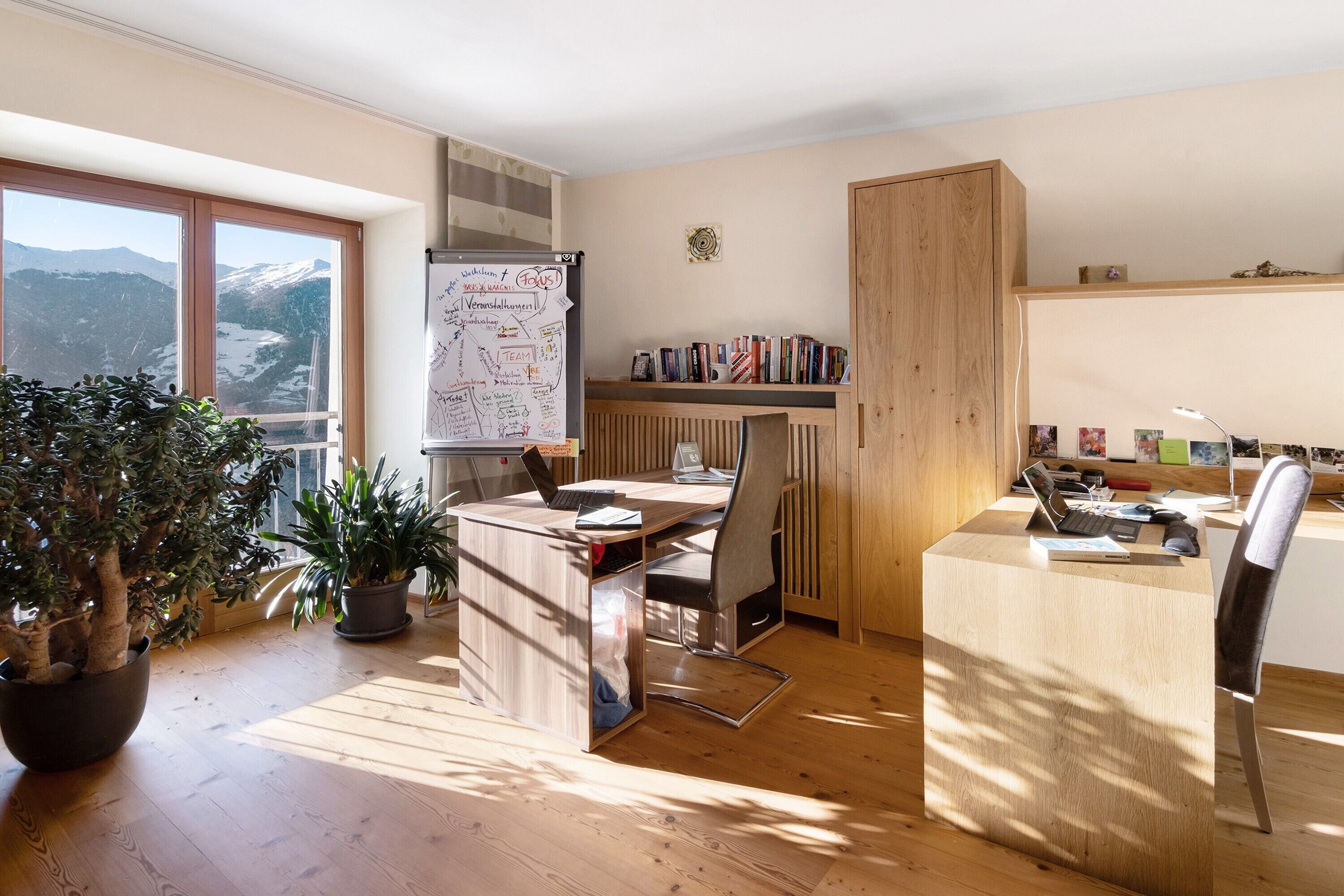 Un bureau moderne comprenant un bureau, une chaise, des plantes en pot, un tableau blanc et une bibliothèque.