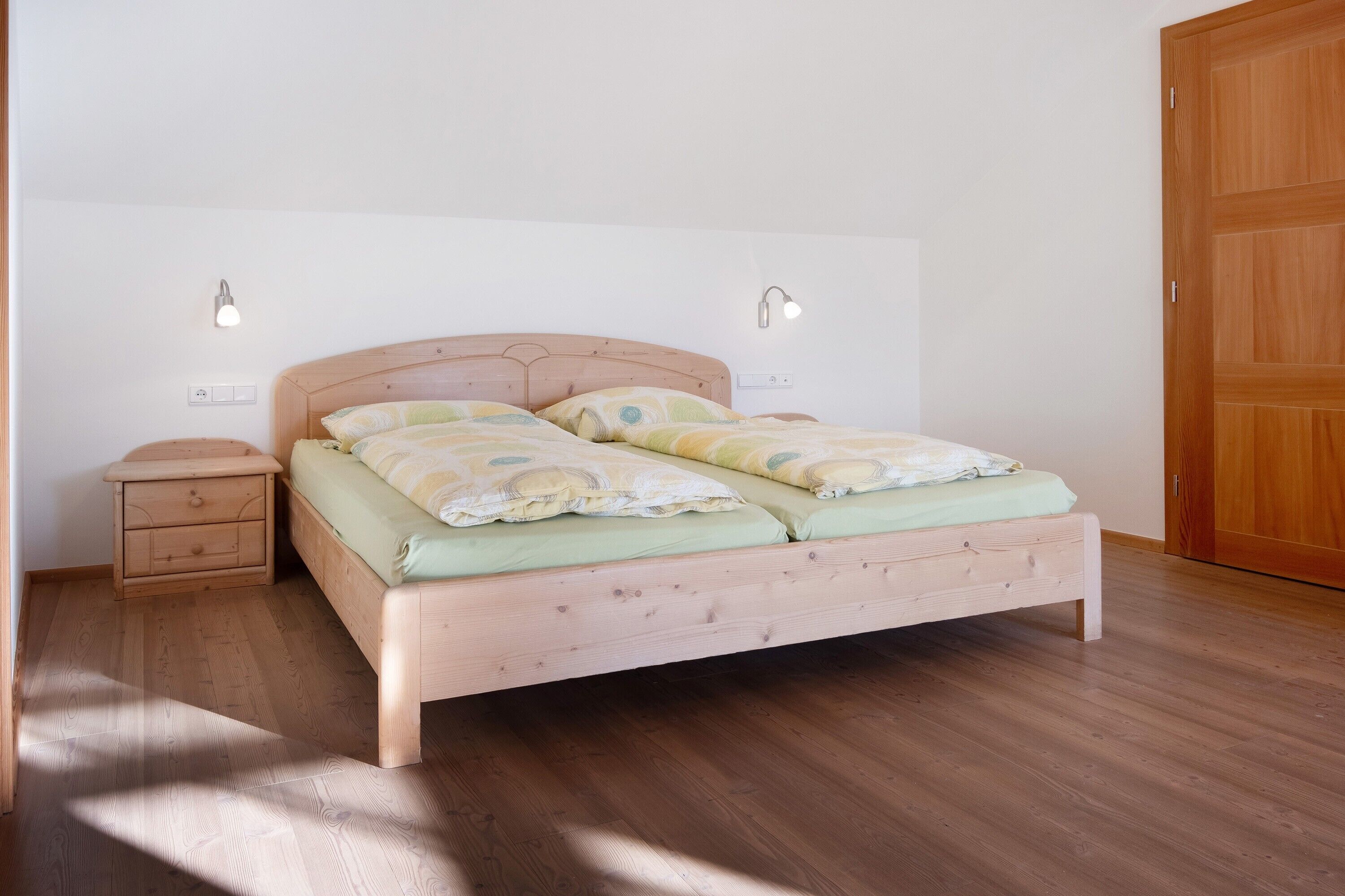 A wooden bed with a headboard, two bedside tables, and two wall-mounted lights.