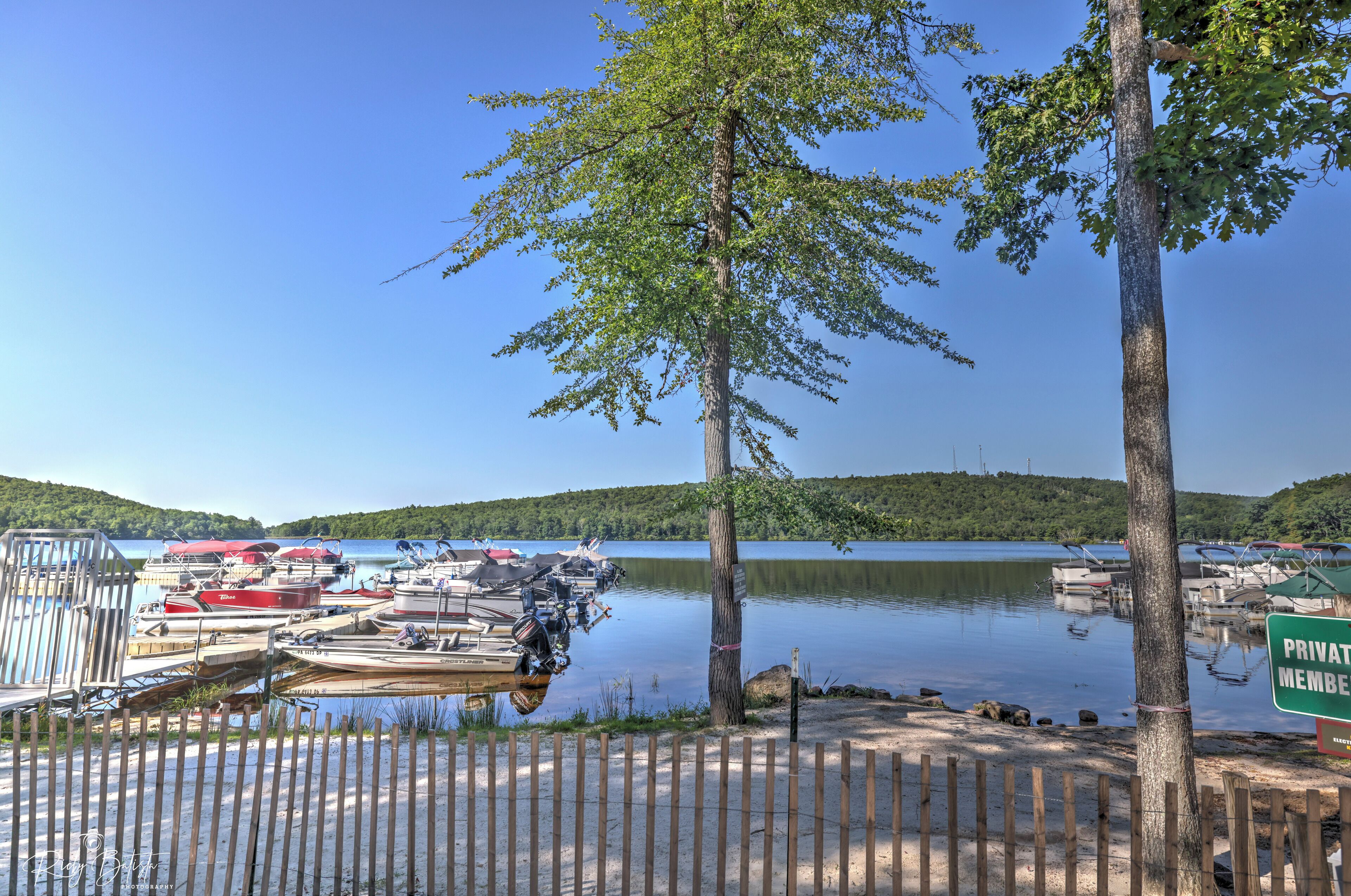 A lakeside dock with boats, a wooden fence, and a sign indicating private membership.