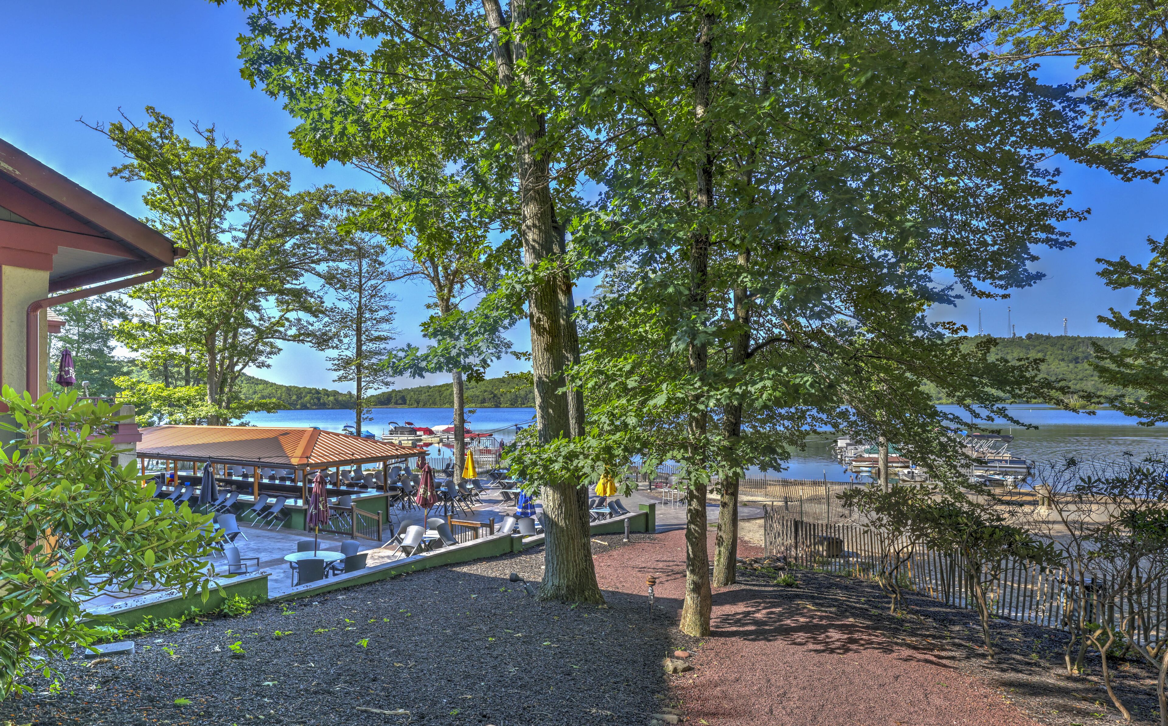 A lakeside outdoor seating area with tables and chairs, surrounded by trees and overlooking a calm lake.