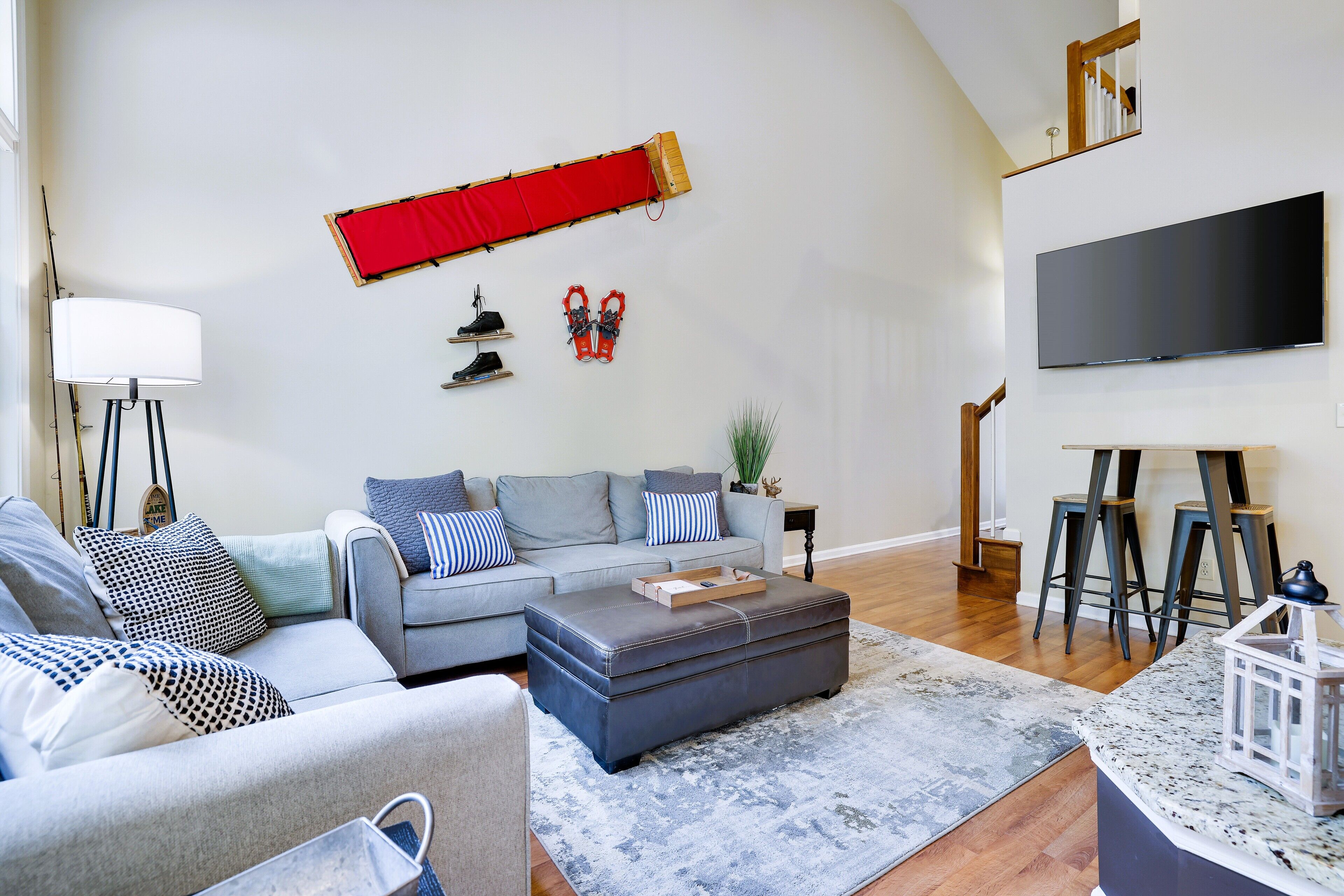 Una sala de estar con un sofá gris, un reposapiés y un televisor de pantalla plana montado en la pared.