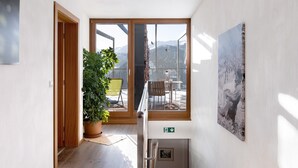 Ein Flur mit einem Blumentopf, Holztüren, einer Glastür, die auf einen Balkon mit Tisch und Stühlen führt, und einem gerahmten Bild an der Wand.
