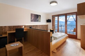 A modern room with a wooden desk, a bed, a small table, and a large window with a mountain view.