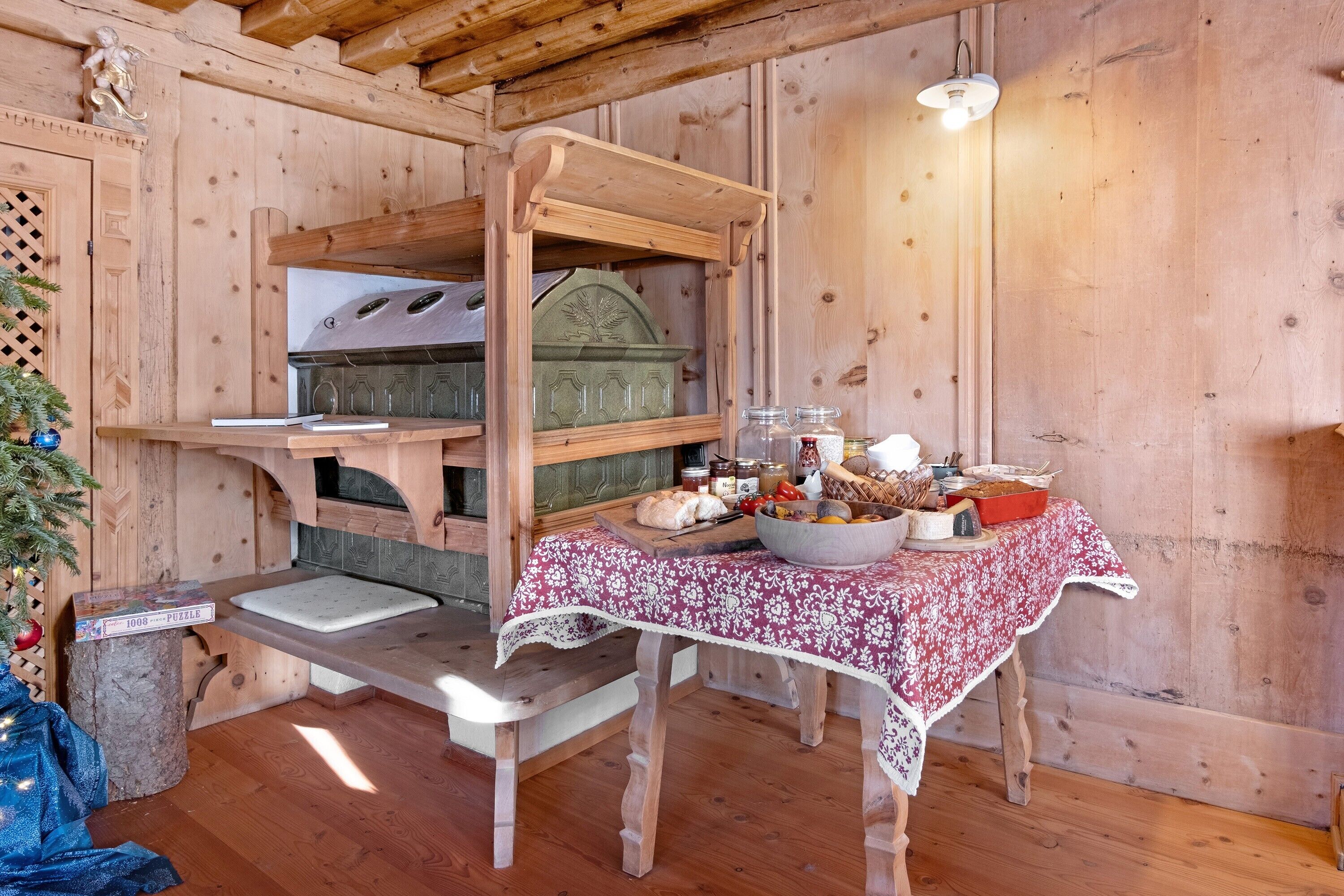 A rustic wooden interior with a wooden table set for a meal, a pizza oven, and a Christmas tree.