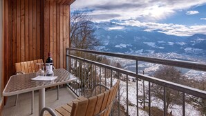 Ein Holzbalkon mit Tisch und Stühlen mit Blick auf eine verschneite Berglandschaft.