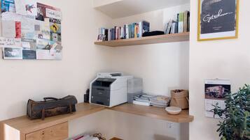 Un espacio de trabajo con un tablón de anuncios, estanterías llenas de libros, una impresora y un escritorio con un bolso antiguo.