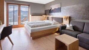 A modern bedroom with a bed, a sofa, a wooden coffee table, and a view of mountains through a sliding door.