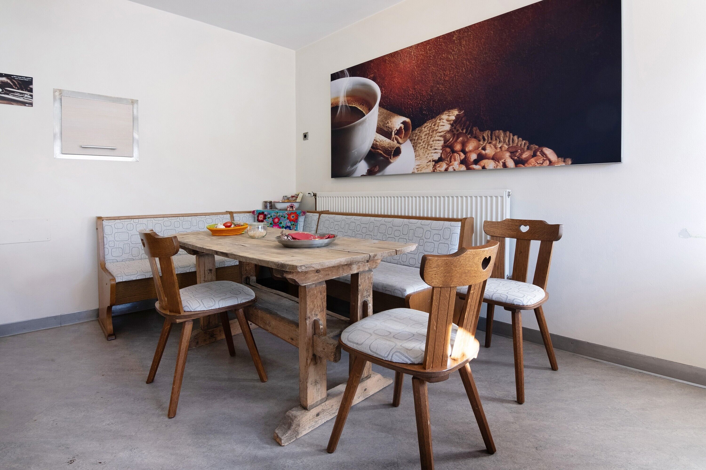 Ein Essbereich mit Holztisch und -stühlen, einem Heizkörper und einem großen Gemälde mit Kaffeemotiv an der Wand.