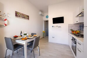 A modern kitchen with a flat-screen TV, a dining area with a table set for two, and a living area with a sofa and a coffee table.