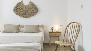 Un dormitorio con cama, mesita de noche, lámpara y sillón.