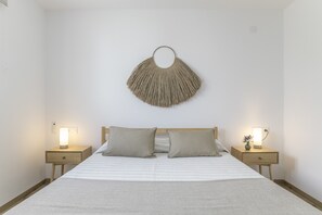 A bedroom with a bed, two bedside tables with lamps, a wall-mounted light fixture, and a wooden headboard.